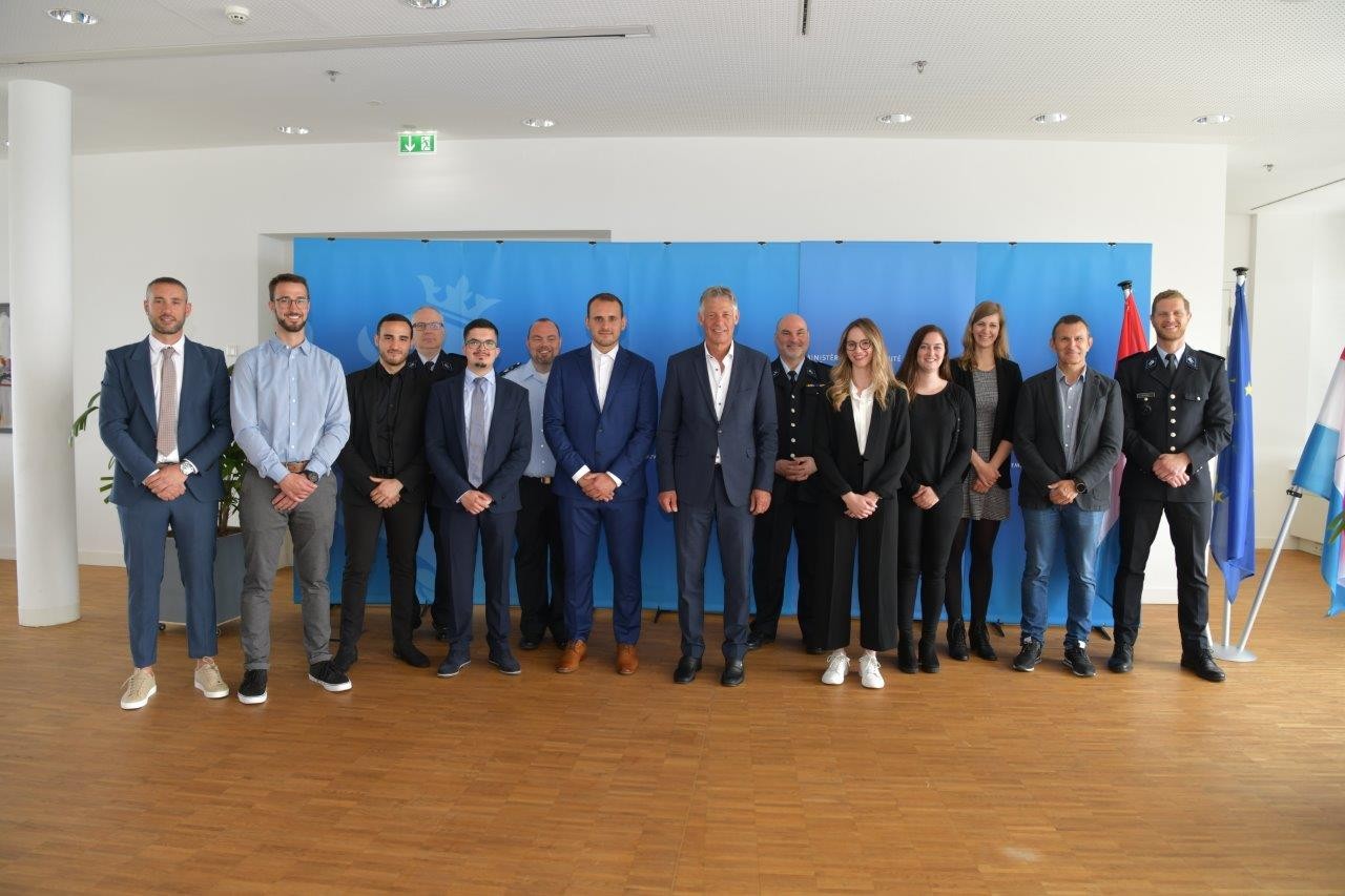 (de g. à dr.) Dany Dos Santos Gonçalves; Joé Meyers; Gil Sousa Cardoso; Emmanuel Brück, Commissaire en chef; Marco Dos Santos Coelho; Mike Greisch, Commissaire en chef; Emanuel Da Silva Rocha; Henri Kox, ministre de la Sécurité intérieure; Patrick Hoffmann, Commissaire en Chef; Anja Frantzen; Willemijn Van Heesen; Célia Limpach; Yves Marson, premier commissaire divisionnaire; Bob Zovilé, directeur adjoint des ressources humaines de la Police grand-ducale