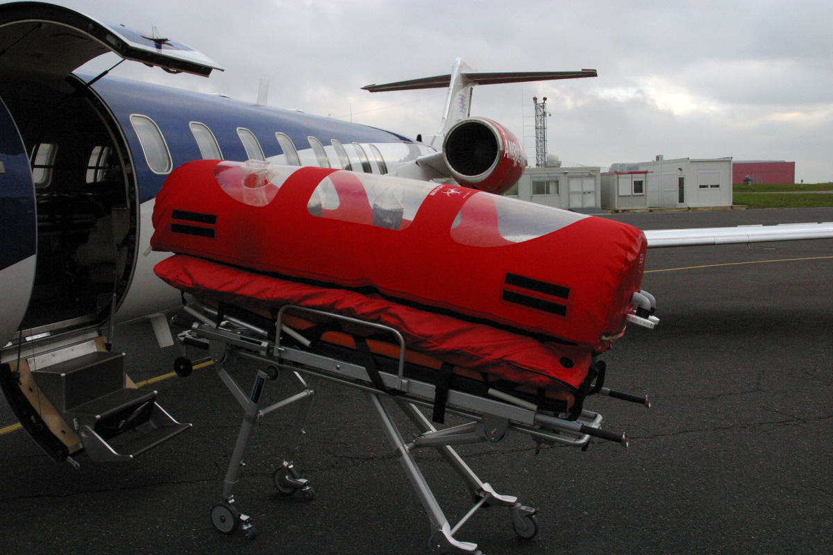 Brancard bulle, destiné au transport en isolement de patients Ebola, devant un avion LearJet adapté de Luxembourg Air Rescue (LAR)
